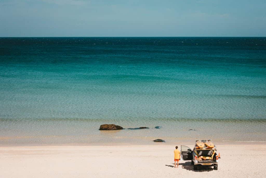 A lifeguard stands by a vehicle on the serene sandy beach of St Ives, England under clear skies.