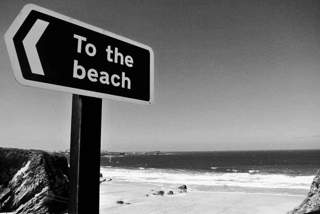 Black and white photo of a 'To the Beach' sign with stunning ocean view at Cornwall, UK.